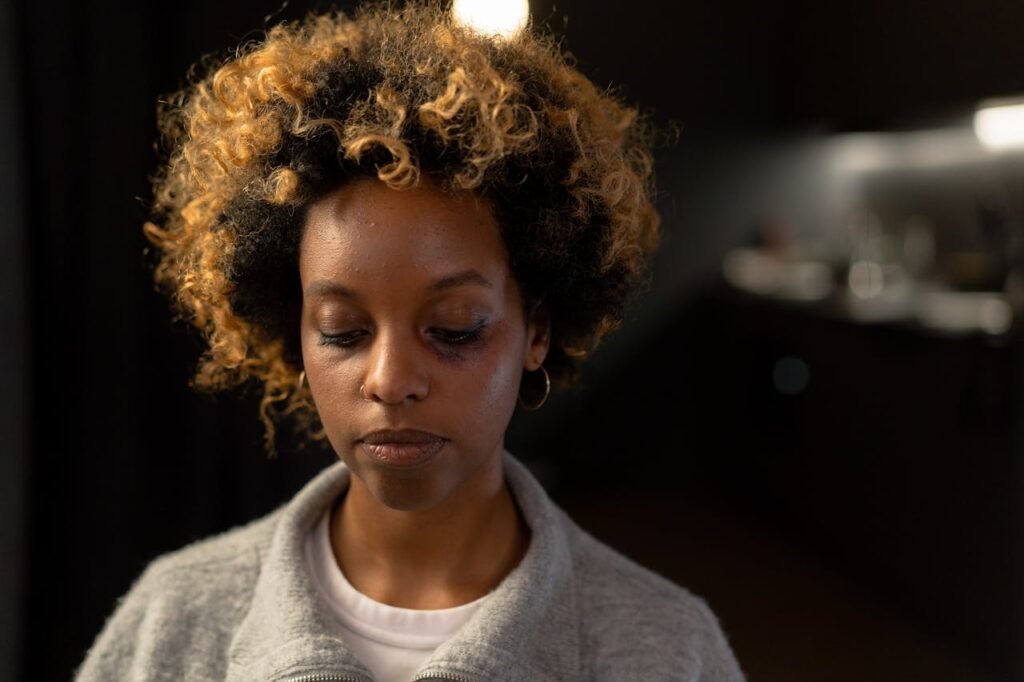 A woman with a bruise on her face, looking thoughtful in an indoor setting.